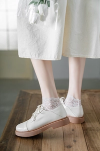 Detail of white floral lace socks paired with matte Oxford shoes on a wooden background