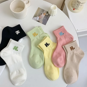 Detail of cotton socks with ribbed cuffs and H. letter embroidery in various pastel colors