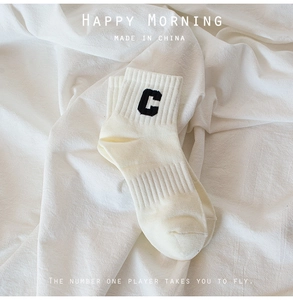 Detail of a creamy white cotton sock featuring a black letter C embroidery on ribbed fabric