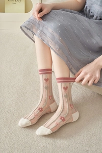 Detail of sheer mesh socks with pink heart and flower embroidery on cream background
