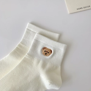 Close-up of white cotton socks featuring a brown bear embroidery and ribbed cuff texture