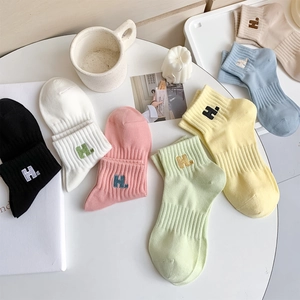 Pastel cotton socks with embroidered H letter in various colors on a minimalist background