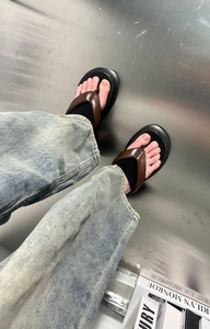 Close-up of thick platform flip-flops with wide dark brown leather straps on a model