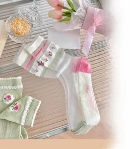 Detail of sheer summer socks with floral embroidery and ruffle cuffs on glass surface