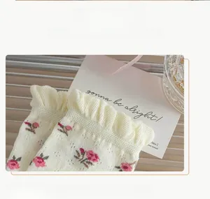 Detail of white cotton mid-calf socks featuring pink floral patterns and elastic ruffled cuffs