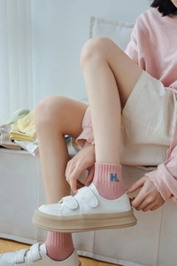 Close-up of pink ribbed cotton socks featuring blue embroidered H letter on the ankle