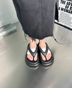 Close-up of minimalist black platform flip-flops with thick soles on industrial background