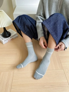 Detail of light gray mid-calf ribbed socks with white stripes on a wooden floor