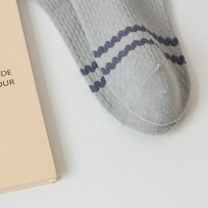 Detail of light gray knit sock featuring purple wavy stripes and breathable mesh texture