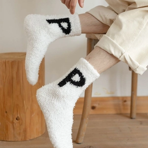 Close-up of thick white coral fleece socks featuring a black knitted P letter detail