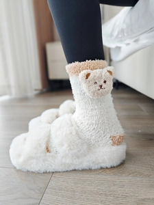 Détail de chaussettes ours en polaire corail et chaussons en peluche sur parquet