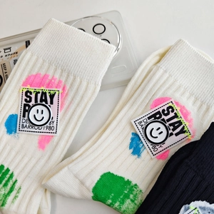 Detail of white ribbed crew socks featuring colorful paint splatters and a smiley button