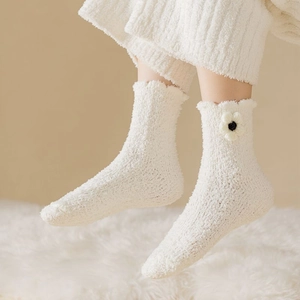 Close-up of white coral fleece socks with floral detail and petal edge on plush rug