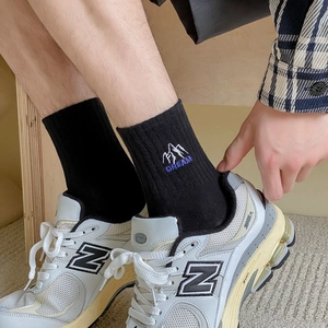 Detail of black cotton socks with white mountain and DREAM embroidery worn with sneakers