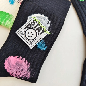 Detail of black mid-calf socks with spray paint patterns and Stay Real embroidered patch