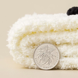 Close-up of white plush coral fleece socks with fluffy pom-poms and thick thermal texture