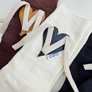 Close-up of knit mid-calf socks with heart leather patches and ribbon bow ties