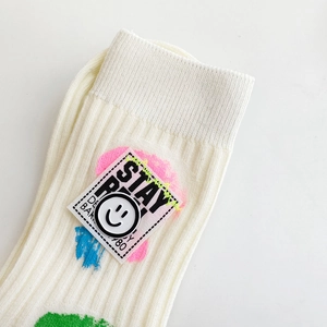 Detail of cream rib-knit socks with smiley patch and multicolor paint splatter design