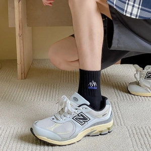 Classic grey and white New Balance 2002R sneakers with embroidered socks on a person