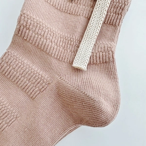 Macro shot of dusty pink ribbed knit socks featuring a white decorative cord detail