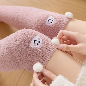 Close-up of pink coral fleece over-the-knee socks with cute pom-poms and smiley face detail