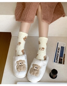 Close-up of cozy white coral fleece slippers and socks with cute brown bear embroidery