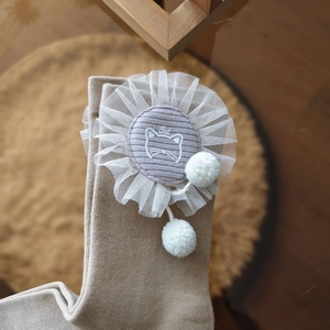 Close-up of beige knit sock with lace flower patch, cat print and white plush pom-poms