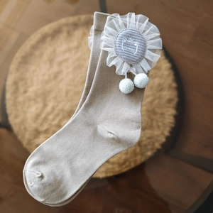 Detail of khaki crew socks with white lace trim, cat embroidery and small pompoms