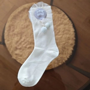 Detail of white cotton socks featuring lace trim, cat embroidery, and blue pom-poms