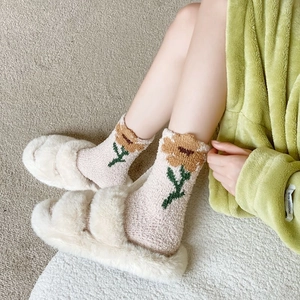 Dettaglio di pantofole in peluche crema e calze termiche a fiori in maglia accogliente