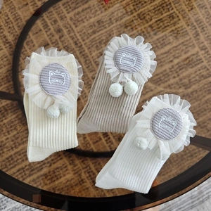 Detail of white cotton baby socks featuring lace trim, cat embroidery and pom poms