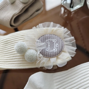 Detail showing knit ribbed cotton socks with cute cat patch, lace trim and plush pom-poms