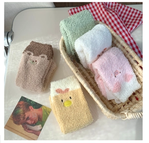 Nahaufnahme dicker Korallenfleece-Wintersocken mit Tierstickerei in einem gemütlichen Korb