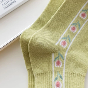 Detailed macro view of green combed cotton socks featuring pink tulip floral embroidery