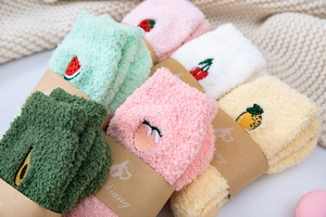 Detailed close-up of fluffy coral fleece socks with fruit embroidery and paper wrap