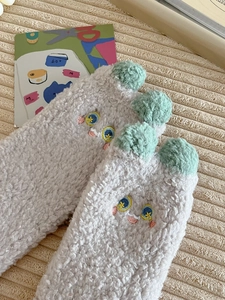 Close-up of warm coral fleece socks with cute cartoon embroidery and green pompoms