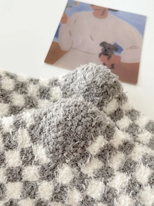 Close-up of thick grey and cream checkered coral fleece socks with a soft plush texture