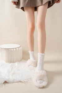 Close-up of beige faux fur cross-band slippers with thick knit warm socks on white rug