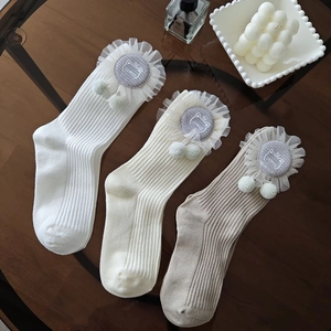 Detailed knit texture of mid-calf socks with cute lace ruffles and plush pom-pom charms