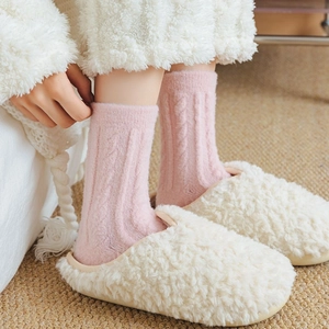 Detail of pink cable knit socks and white fleece slippers on a warm beige carpet