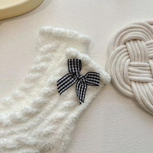 Close-up of white coral fleece socks with black and white checkered bow detail