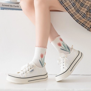 Green floral crew socks with tulip patterns worn with white canvas sneakers and casual skirt