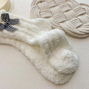 Close-up of white coral fleece socks with cute checkered bow and soft plush texture
