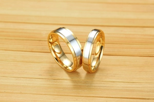 Macro view of gold and silver two-tone stainless steel couple rings on a wooden surface