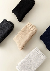 Folded thick wool knit socks in multiple colors with ribbed cuffs on a textured surface