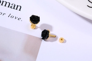Detail of elegant black rose stud earrings with golden base on a magazine background