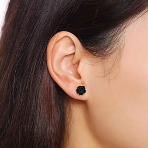 Close-up of elegant black rose stud earrings with gold base worn on the ear