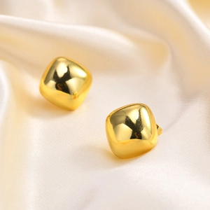 Macro view of square 18K gold plated earrings on elegant cream silk fabric background
