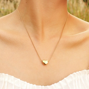 Elegante ciondolo a cuore dorato su una sottile catena a serpente indossata da una donna