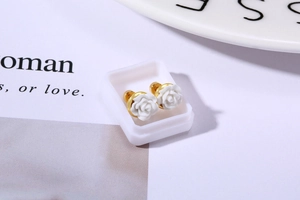 Macro detail of white rose earrings with gold metal base on minimalist background
